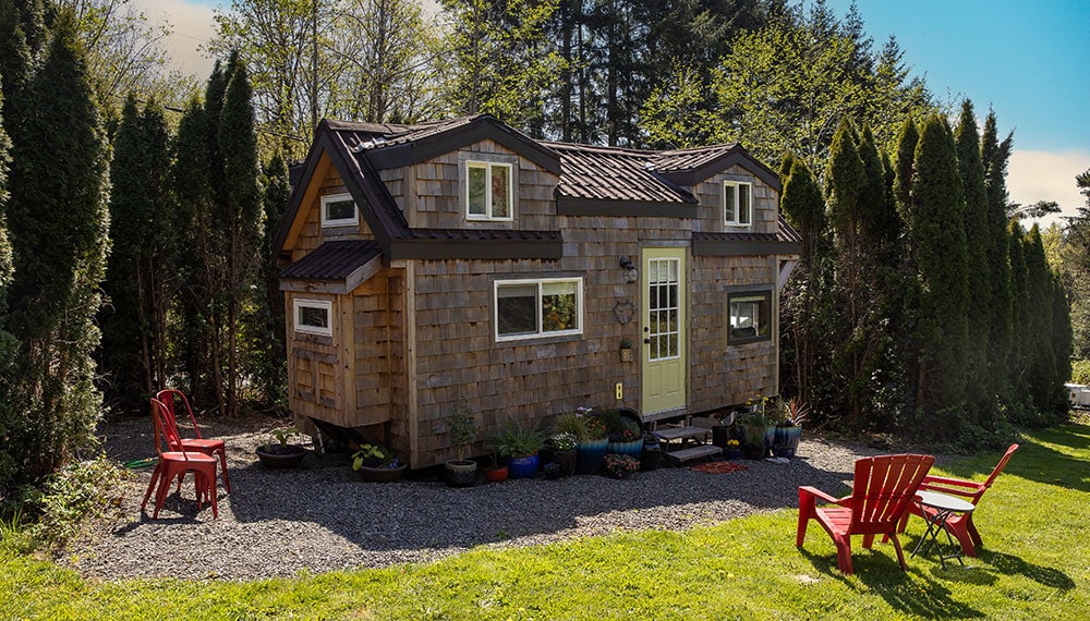 Tiny home in backyard with gravel around it and chairs